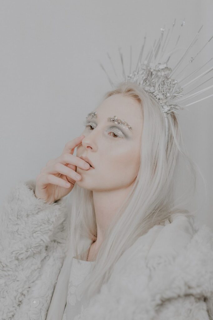 Blonde woman dressed in white and wearing glitter makeup and crown