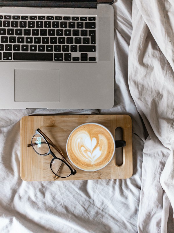 a macbook with a wooden board with glasses and a flat white on top